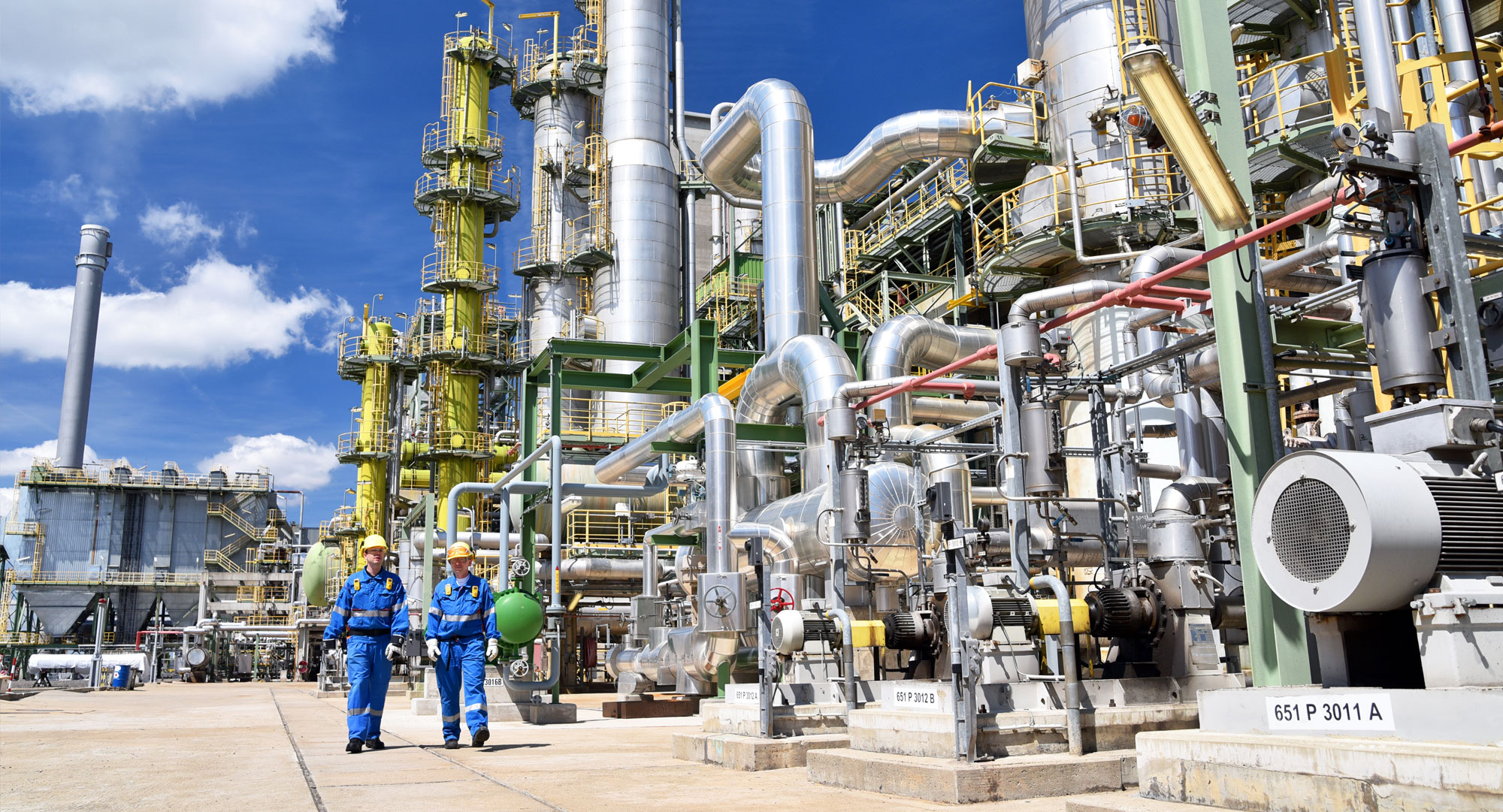 2 Personen stehen vor einer großen Industrieanlage bei schönen und sonnigen Wetter