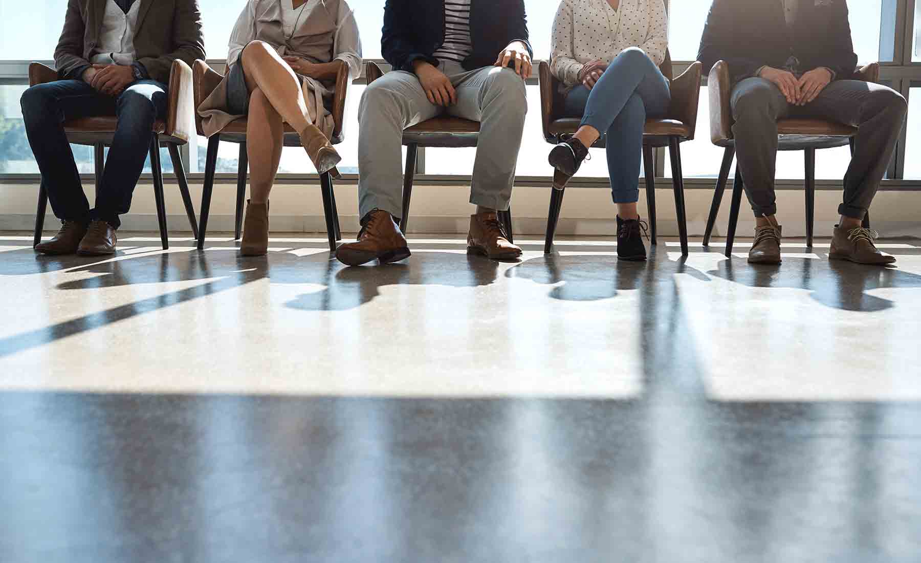 Personen sitzen auf Stühlen und warten auf ihr Bewerbungsgespräch